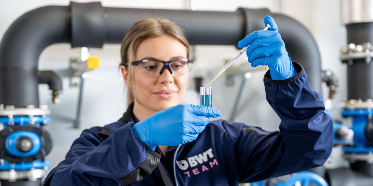 BWT Servicetechnikerin entnimmt eine Wasserprobe an einer industriellen Wasseranlage zur Legionellenanalyse.