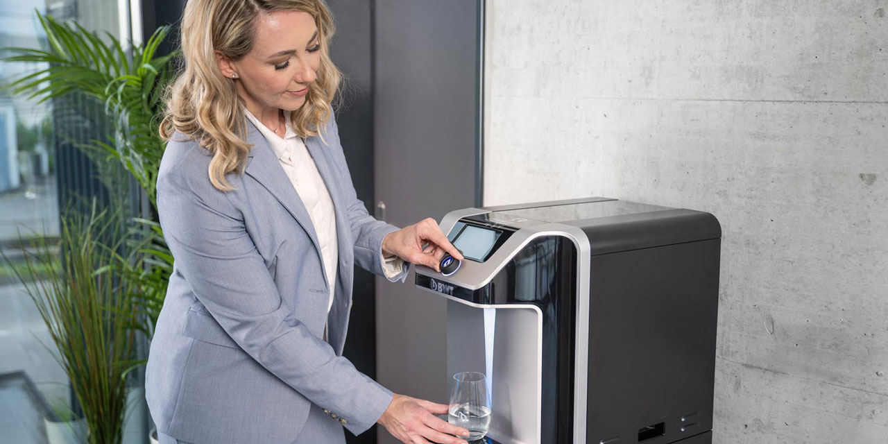 Frau bezieht Wasser an einem Wasserspender.