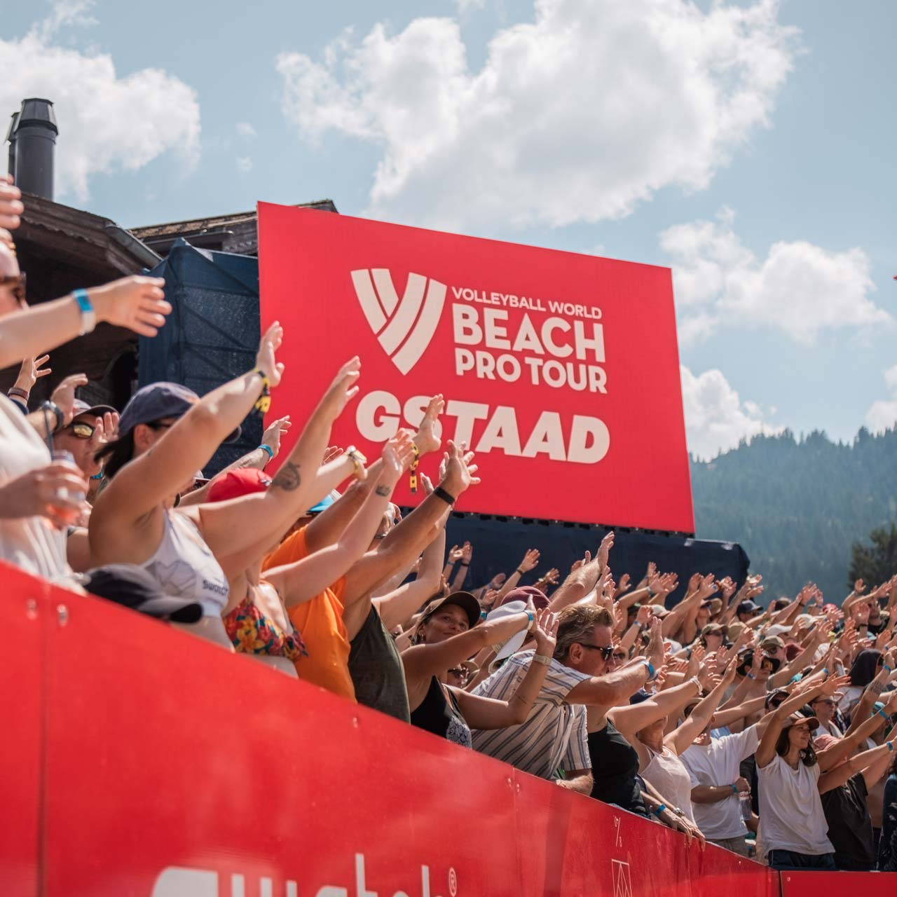 Publikum halt Hände hoch in Stadion, vor roter Leinwand.