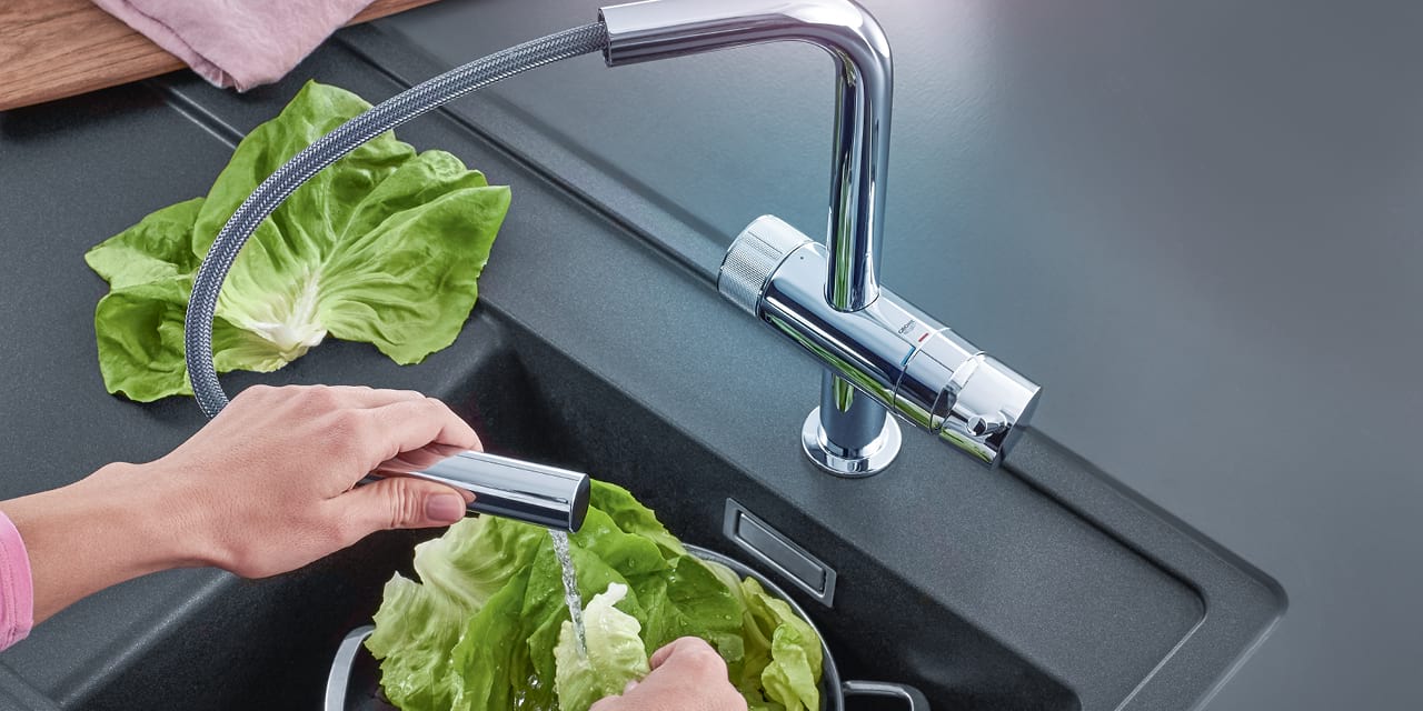 Hand hält ausziehbare Spülbrause der AQA drink Pure LOFT Küchenarmatur und wäscht Salat.