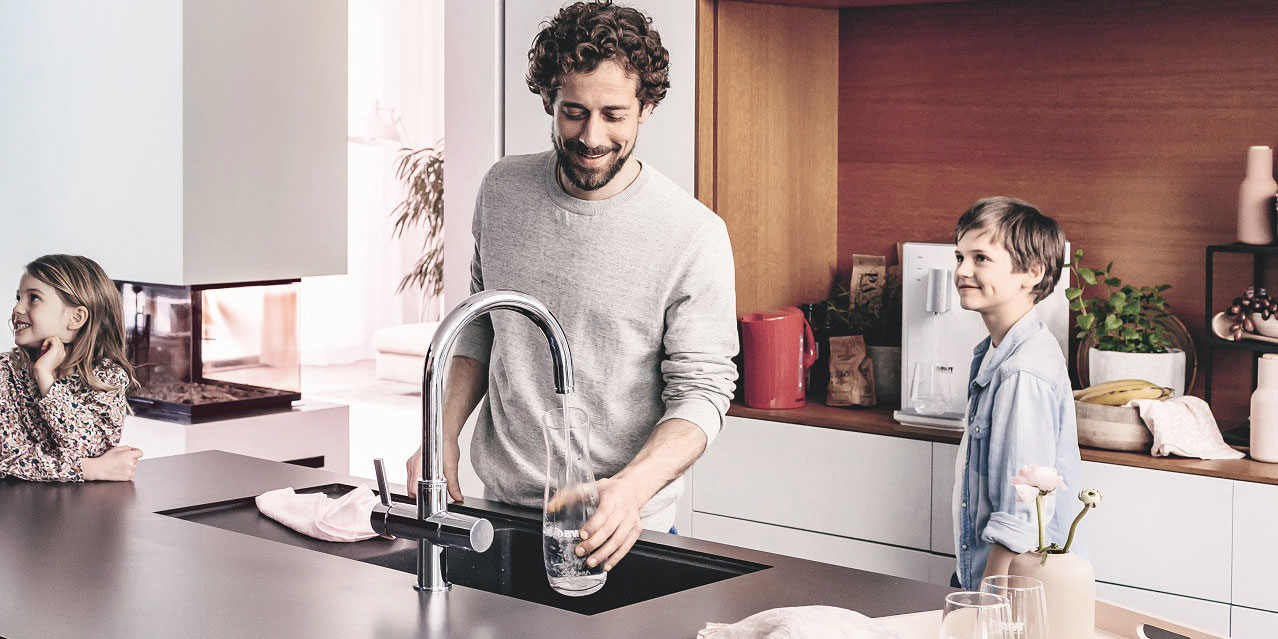 Un homme laisse couler de l'eau d'un robinet de cuisine BWT.