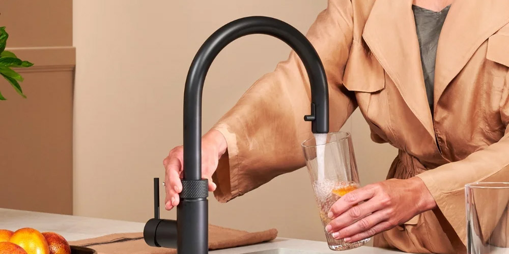 Une personne se tient au robinet et remplit un verre d’eau.