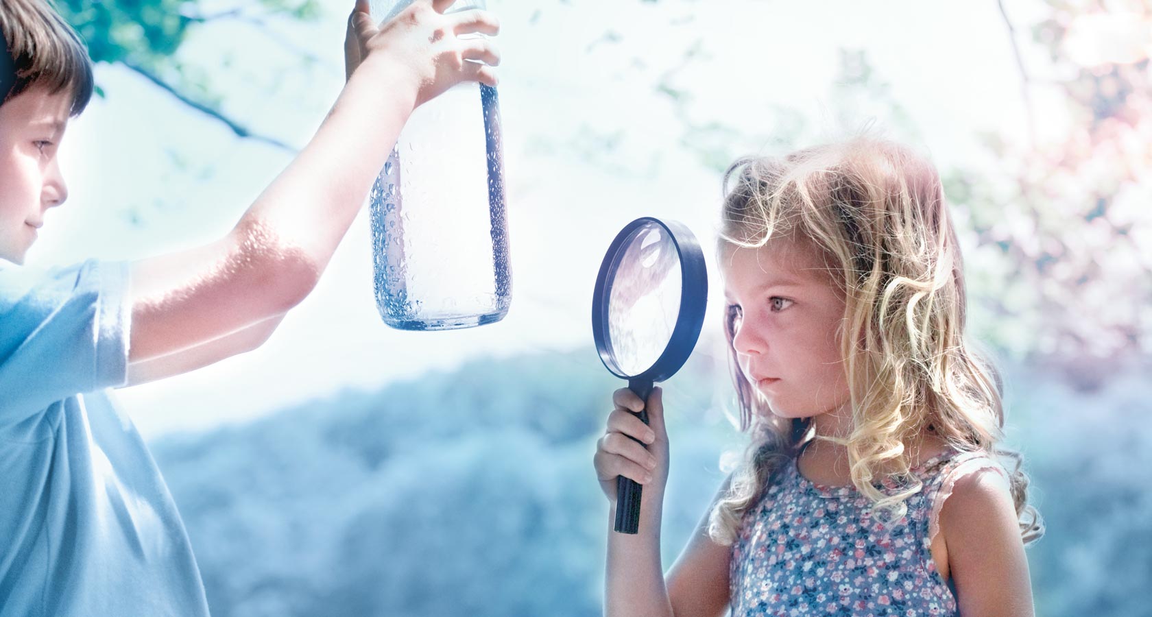 Une fillette regarde une bouteille d'eau avec une loupe.