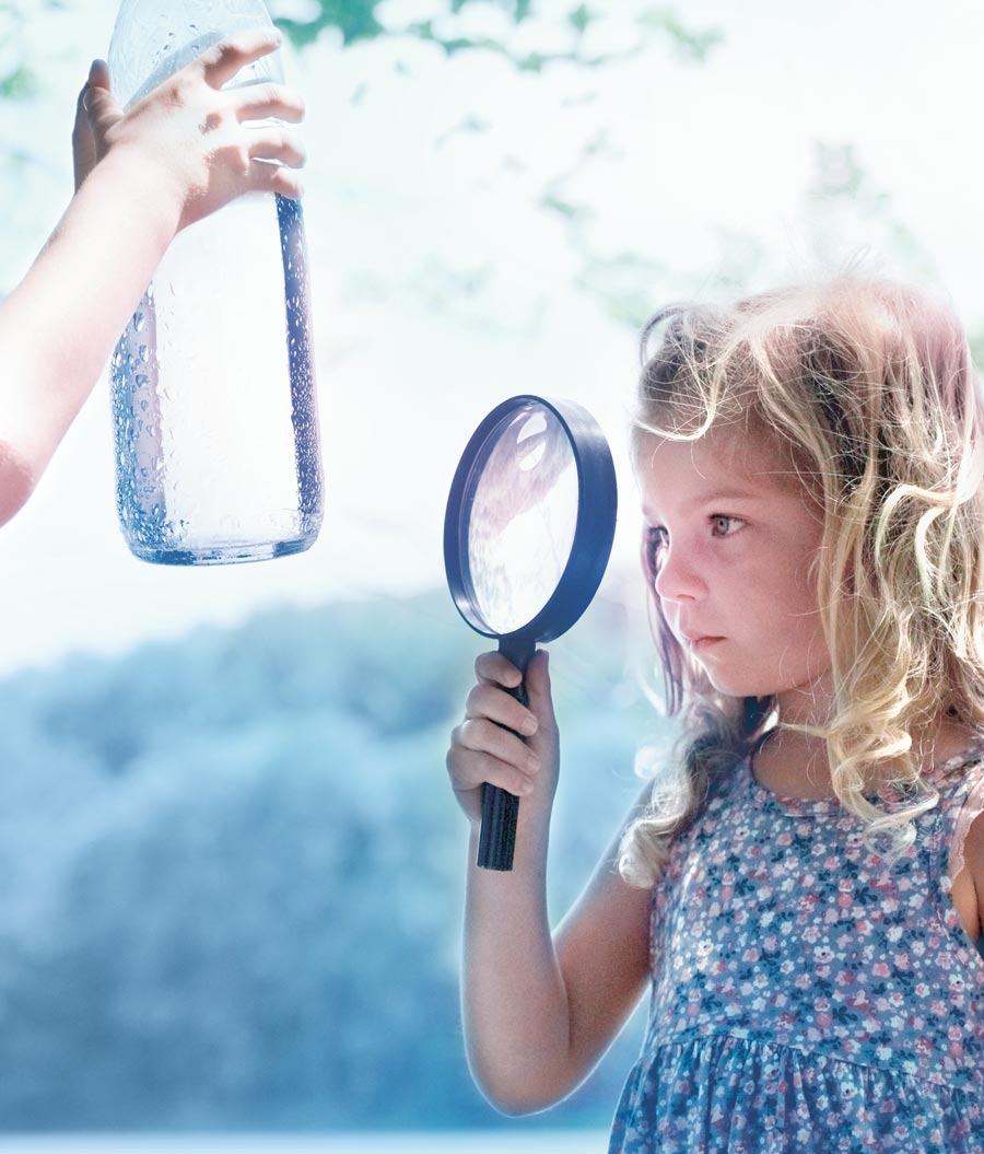 Une fillette regarde une bouteille d'eau avec une loupe.