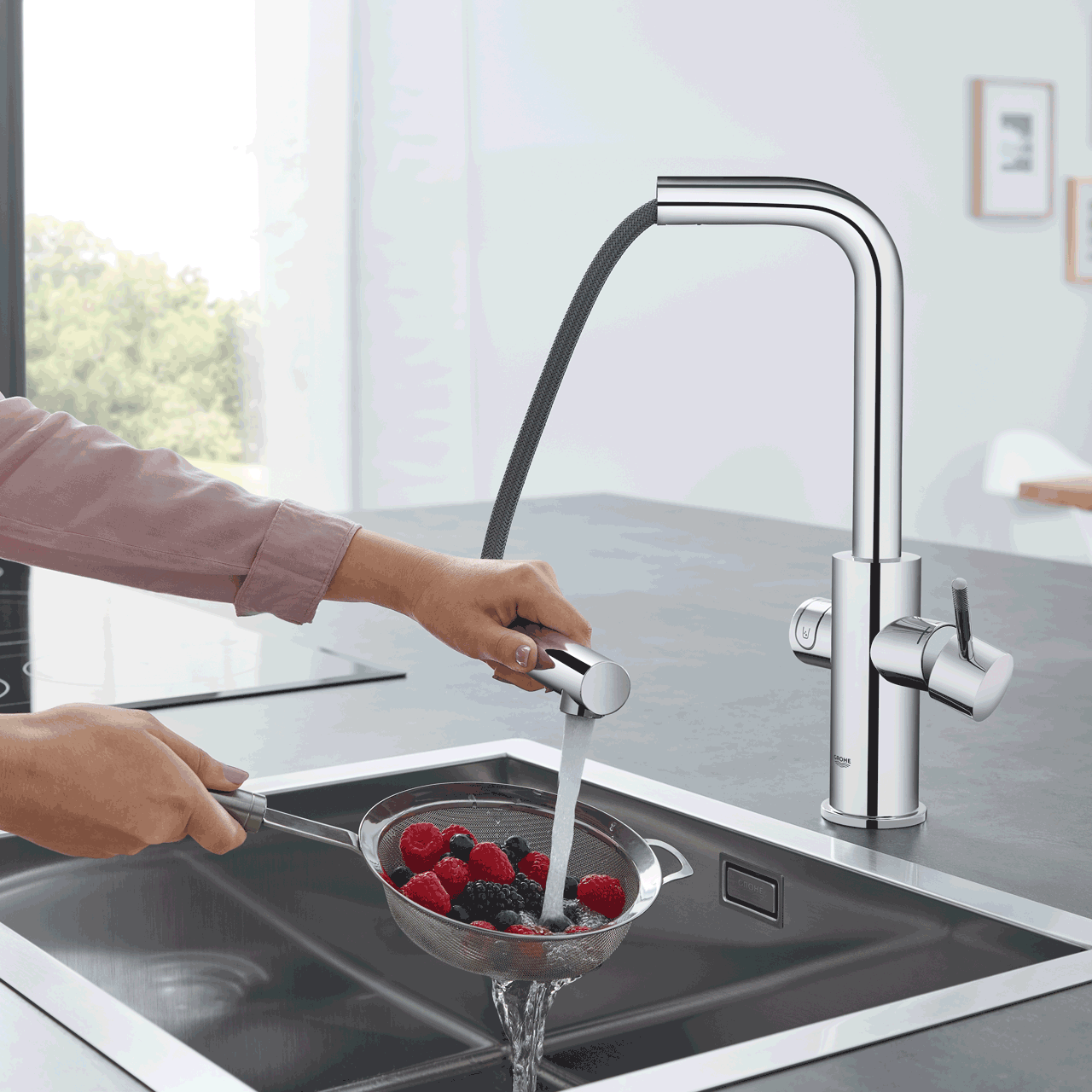 Une femme rince des baies avec l'eau d'une douchette extractible.