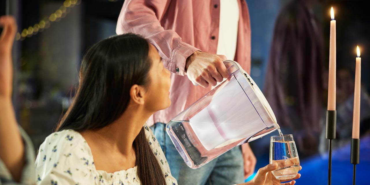 Un homme verse de l'eau d'une carafe filtrante BWT dans le verre d'une femme.