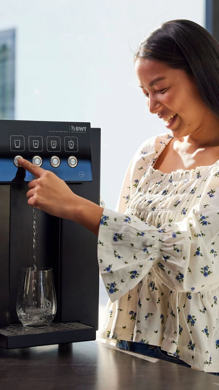 Frau füllt Wasser aus Wasserspender in Trinkglas