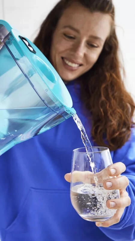 Frau mit blauem BWT Tischwasserfilter und Glas