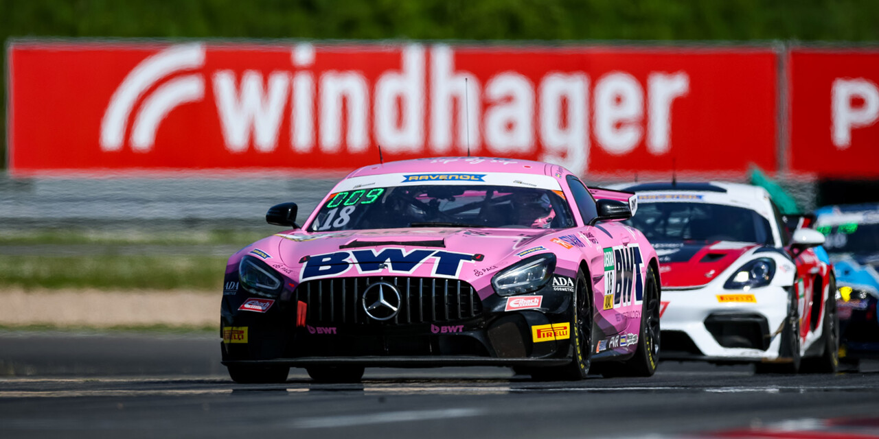 A vibrant pink BWT-branded Mercedes AMG GT3 leads the pack on a professional racetrack.