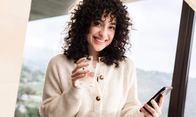 A woman holds a glass of water and a cell phone in her hands.