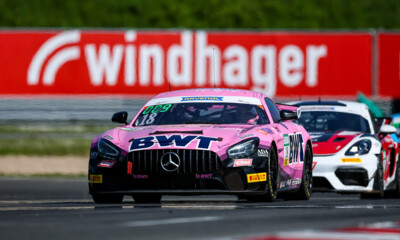 A vibrant pink BWT-branded Mercedes AMG GT3 leads the pack on a professional racetrack.