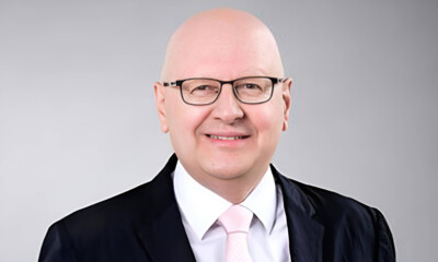 A formal portrait of Andreas Weissenbacher dressed in a dark suit, white shirt, and light pink tie.