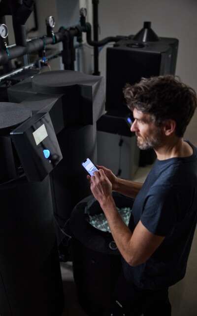 A technician interacts with a smartphone in front of a modern control panel for water filtration in an industrial plant.