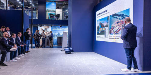 A professional presenter delivers a business presentation to an attentive audience at a modern trade show booth.