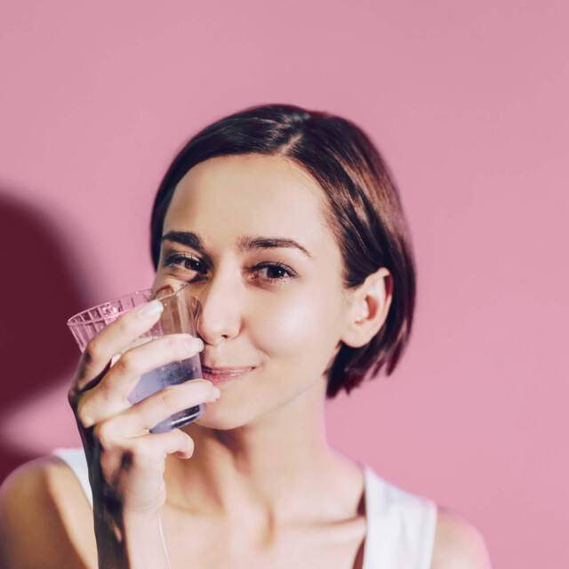 A woman with glass in front of a pink background.