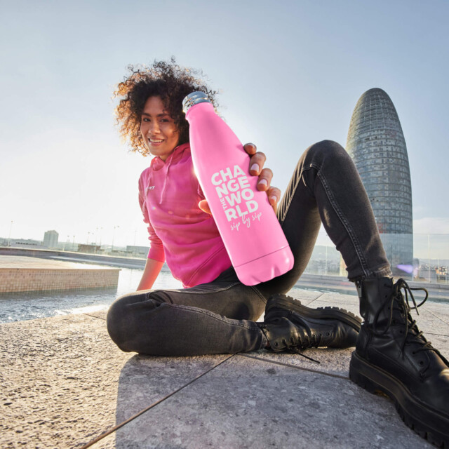 A woman with a pink BWT water bottle on a square in front of a skyscraper. 