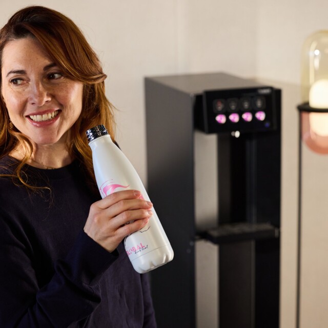 A woman holds a water bottle in her hand and stands in front of a water dispenser.